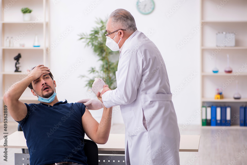 Obraz premium Young male patient visiting old male doctor in vaccination conce