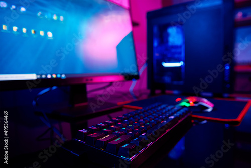 PC with rgb keyboard for gaming computer video games with neon colored background, dark room with game workplace without people