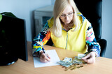 A middle-aged thoughtful woman counting euro money and takes notes at a desk in the home office