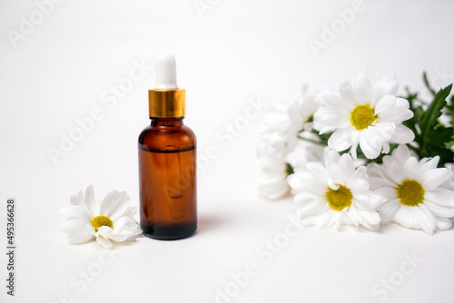 A brown glass bottle with essential oil and a chamomile flowers. White background. Copy space. The concept of organic natural cosmetics