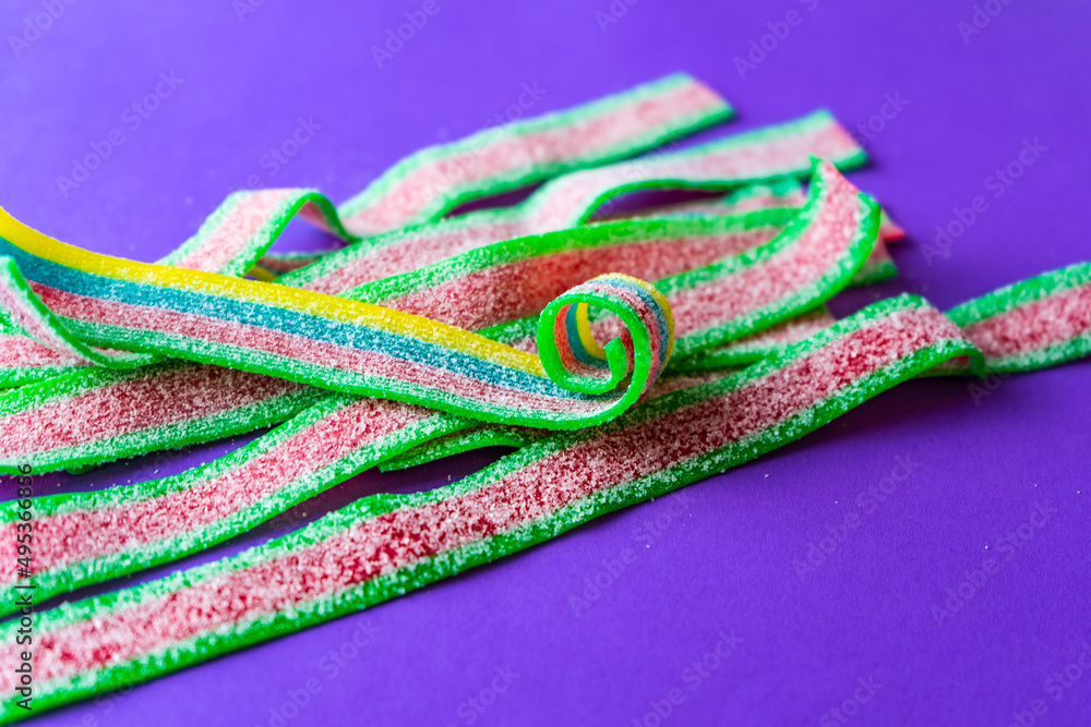Rainbow stripes of sour jelly candies in sugar sprinkles on a purple