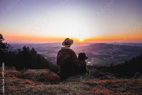 Man in hat and dog sitting outside watching sunset. thinking and relaxing.