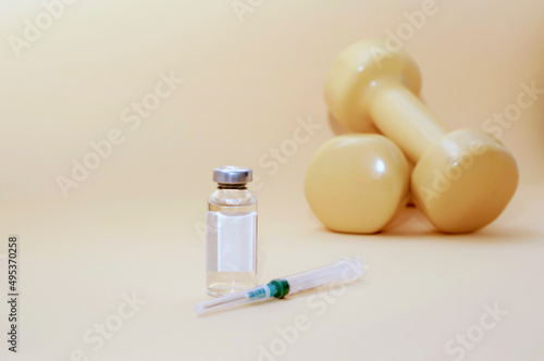 syringe and a jar of liquid stand next to dumbbells on a yellow background, horizontal picture, copy space. the concept of doping in sports, steroids, testosterone and other drugs banned in sports. photo