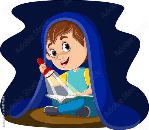 Little boy reading a book at night with flashlight under blanket