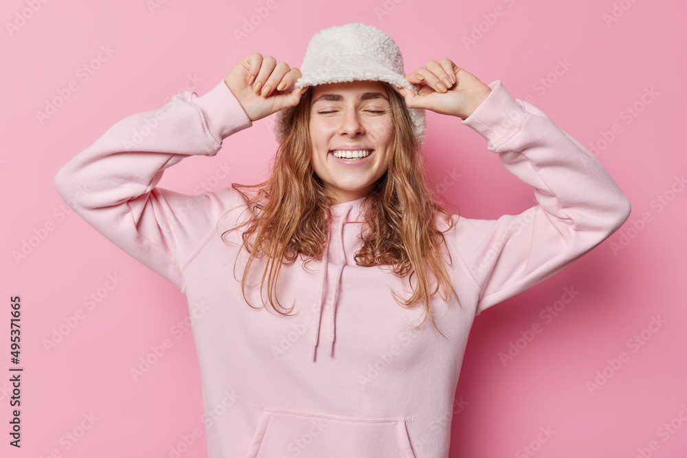 Pretty energetic long haired woman keeps eyes closed smiles broadly wears panama and casual sweatshirt going to have walk isolated over pink background. People sincere emotions feelings concept Pretty energetic long haired woman keeps eyes closed smiles broadly wears panama and casual sweatshirt going to have walk isolated over pink background. People sincere emotions feelings concept