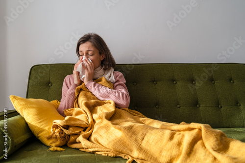 Sick woman blowing nose in facial tissue at home photo