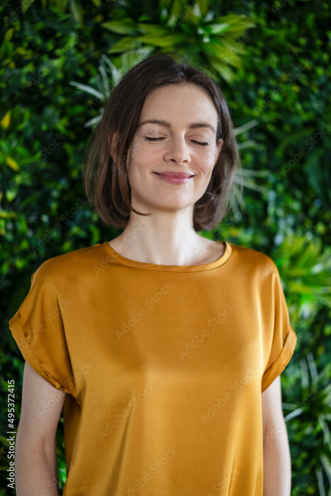 Smiling woman with eyes closed at wall with plants Smiling woman with eyes closed at wall with plants