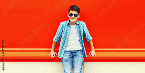 Portrait of teenager boy wearing sunglasses and shirt in the city on red background