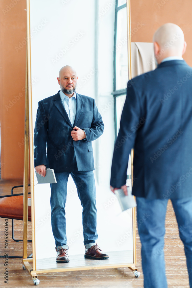 Portrait of serious handsome middle-aged bald man with gray beard wearing blue  suit jacket, jeans, holding notebook, looking at mirror reflection, raising  eyebrow indoors. Business, self-motivation. Photos | Adobe Stock