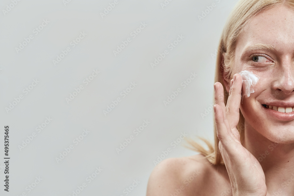 Smiling caucasian guy smear cosmetic cream on face Smiling caucasian guy smear cosmetic cream on face