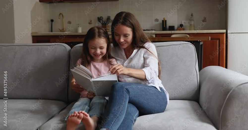 Loving mom read book her little daughter seated on sofa at home. Preschool girl enjoy pastime and fascinating fairytale rest on couch with caring mother. Kids development, intellectual growth concept Loving mom read book her little daughter seated on sofa at home. Preschool girl enjoy pastime and fascinating fairytale rest on couch with caring mother. Kids development, intellectual growth concept