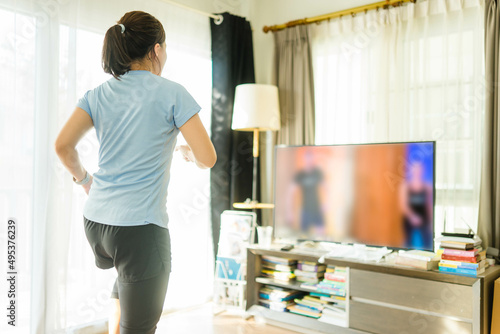 Fototapeta Naklejka Na Ścianę i Meble -  Video streaming Stay home.home fitness workout class live streaming online.Asian woman doing strength training cardio aerobic dance exercises watching videos on a smart tv in the living room at home.