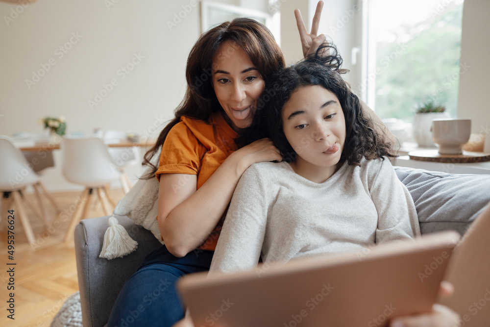 Woman and daughter sticking out tongues taking selfie through tablet PC at home Woman and daughter sticking out tongues taking selfie through tablet PC at home