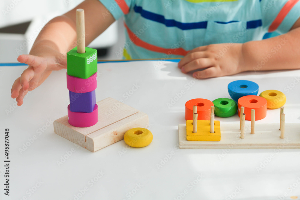A little boy plays with wooden toys and builds a tower. Educational logic toys for children. Montessori games for child development. Children's wooden toy. A little boy plays with wooden toys and builds a tower. Educational logic toys for children. Montessori games for child development. Children's wooden toy.