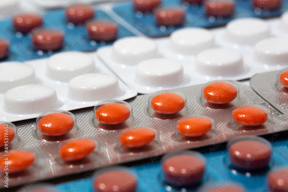 Medicine tablets of different colors are arranged in an orderly manner. Orange colored round pills in selective focus. Medicine tablets of different colors are arranged in an orderly manner. Orange colored round pills in selective focus.