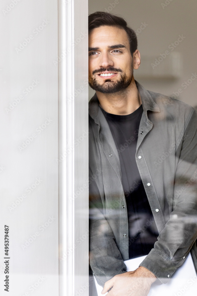 Smiling man leaning on door seen through glass Smiling man leaning on door seen through glass