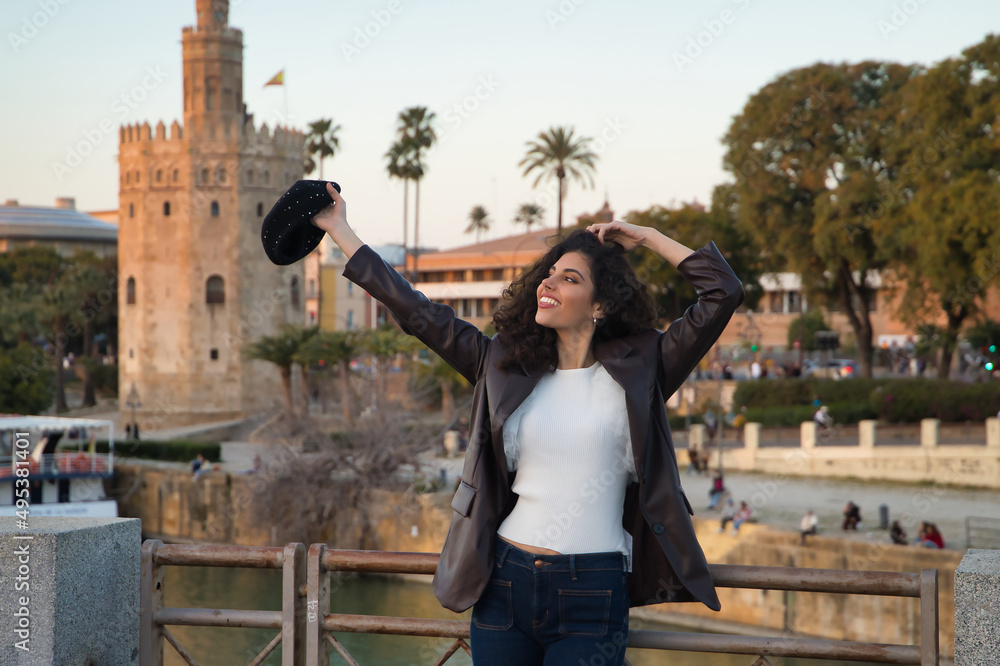 Young and beautiful woman, brunette, with curly hair, with leather jacket and white shirt with a beret in her hand, smiling happily, leaning on the railing of a bridge. Concept holidays, travel. Young and beautiful woman, brunette, with curly hair, with leather jacket and white shirt with a beret in her hand, smiling happily, leaning on the railing of a bridge. Concept holidays, travel.