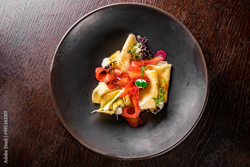 Crepes with smoked gravlax salmon on black plate on wooden table dark background photo