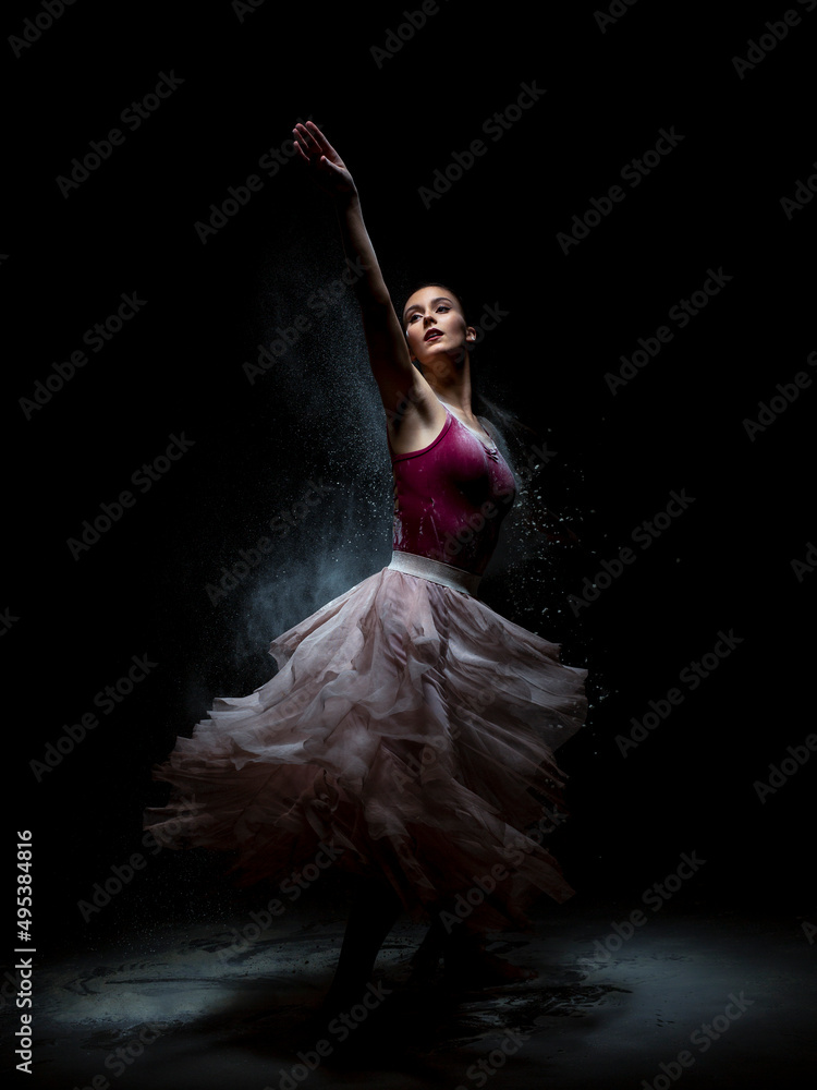 Fototapeta premium Chica joven bailando en movimiento con polvos de harina en dispersión con fondo oscuro. Baile y danza artística.