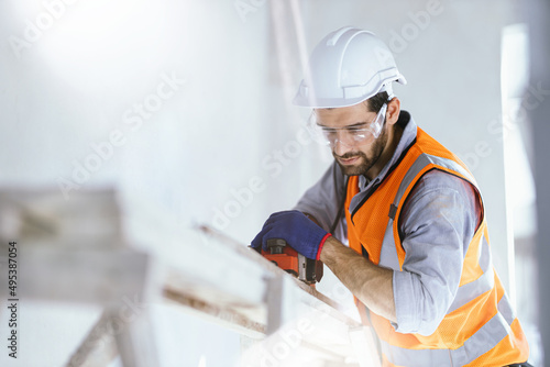 Handsome young white engineer is happily using the tools to build a house.