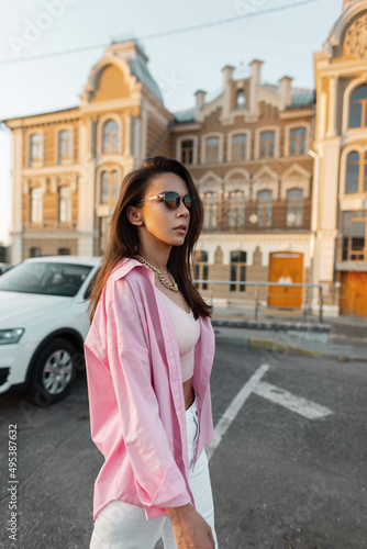 Trendy glamour woman fashion model in sunglasses with pink fashionable shirt walks in the city