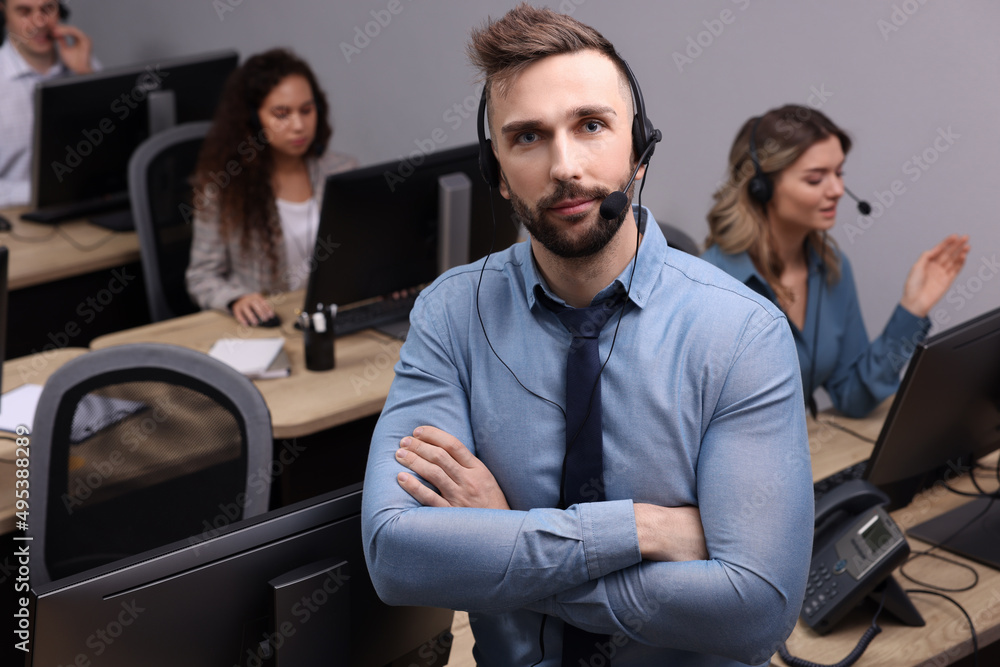 Handsome call center operator with headset and his colleagues working in modern office Handsome call center operator with headset and his colleagues working in modern office