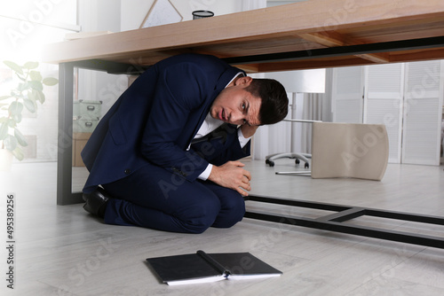 Scared man hiding under office desk during earthquake
