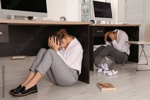 Fototapeta Scared employees hiding under office desks during earthquake
