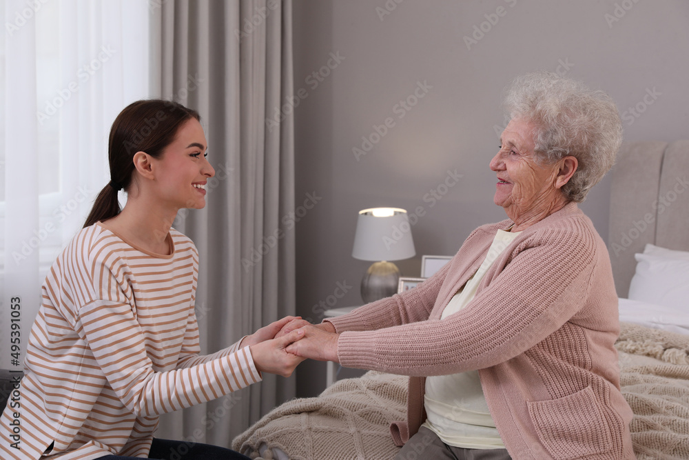 Young caregiver talking to senior woman in bedroom. Home health care service Young caregiver talking to senior woman in bedroom. Home health care service