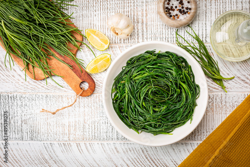 Top view of Sauteed agretti with lemon, italian food. Raw ingredient. Saltwort or salsola soda. White table. photo