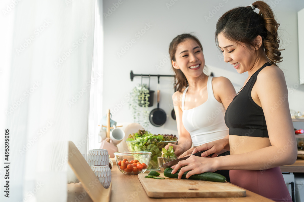 Asian young two women sibling in sportswear cooking salad in kitchen. 