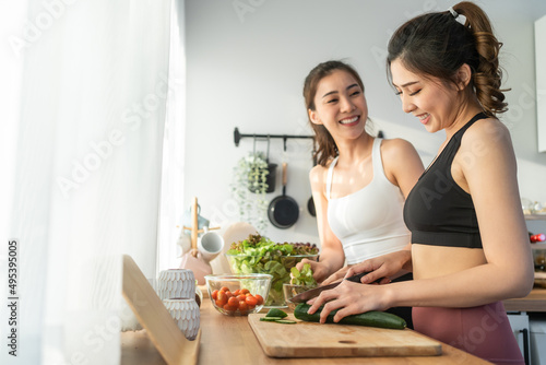 Asian young two women sibling in sportswear cooking salad in kitchen. 