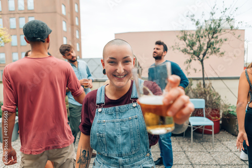 Photography smiling skinhead gender woman cheering with a beer at the rooftop party