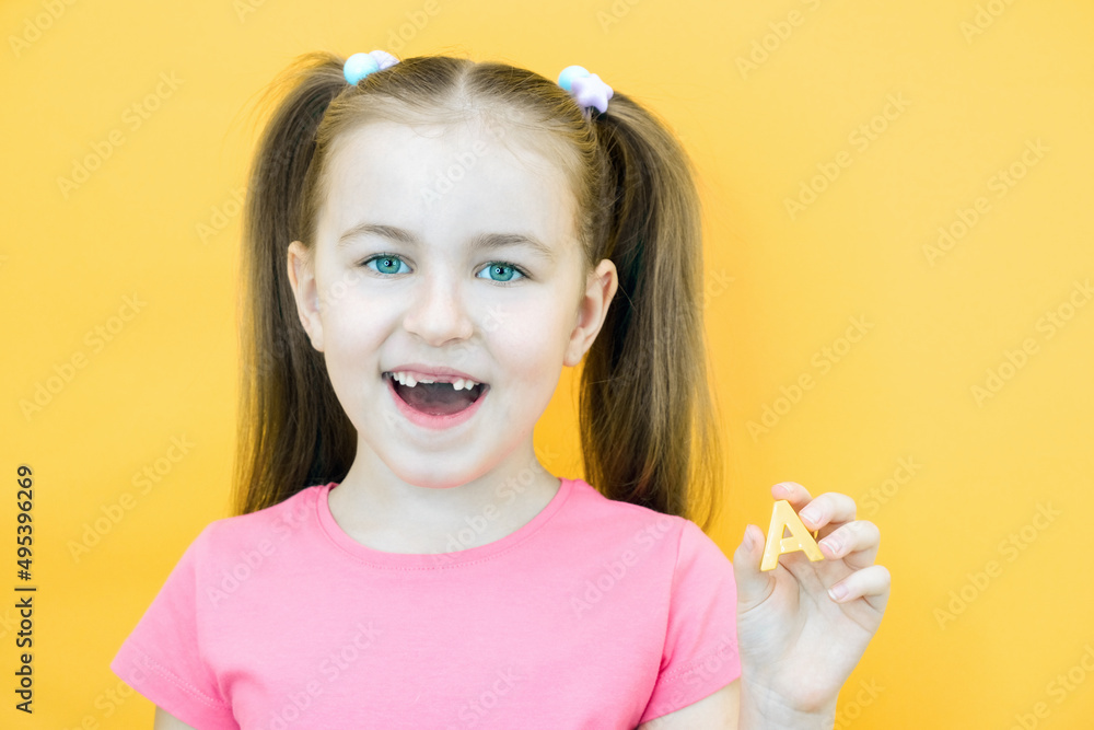 speech therapy. Toddler girl holding the letter A in her hands. Classes with a speech therapist. Girl on isolated yellow speech therapy. Toddler girl holding the letter A in her hands. Classes with a speech therapist. Girl on isolated yellow