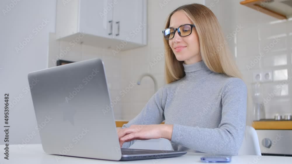 Cheerful white woman typing text on laptop computer in home kitchen. Freelance copy writer person working online. Beautiful Ukrainian female in nerd glasses using notebook pc for work Cheerful white woman typing text on laptop computer in home kitchen. Freelance copy writer person working online. Beautiful Ukrainian female in nerd glasses using notebook pc for work