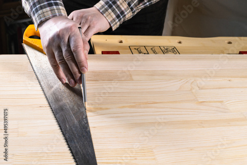 carpenter draws cutting line by pencil on wooden board with hand saw blade on workbench at home