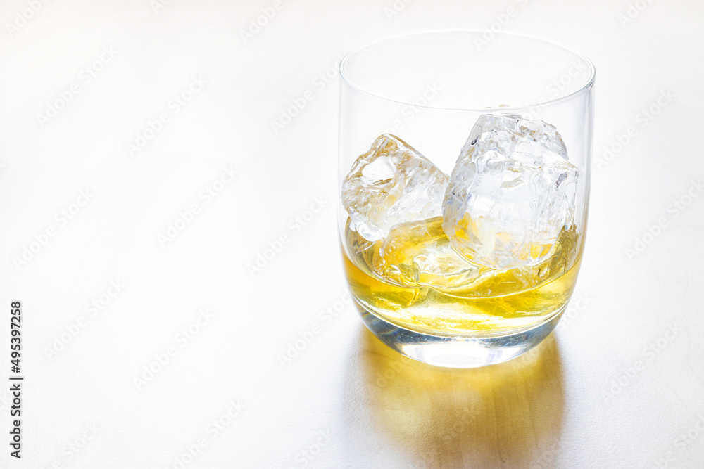 side view of portion single malt scotch whisky on the rocks in glass on pale table with copyspace side view of portion single malt scotch whisky on the rocks in glass on pale table with copyspace