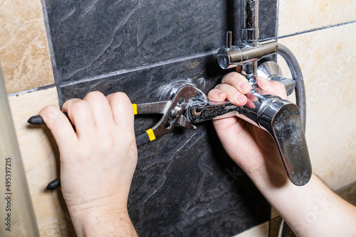 plumber unscrews shower faucet on tiled wall at home