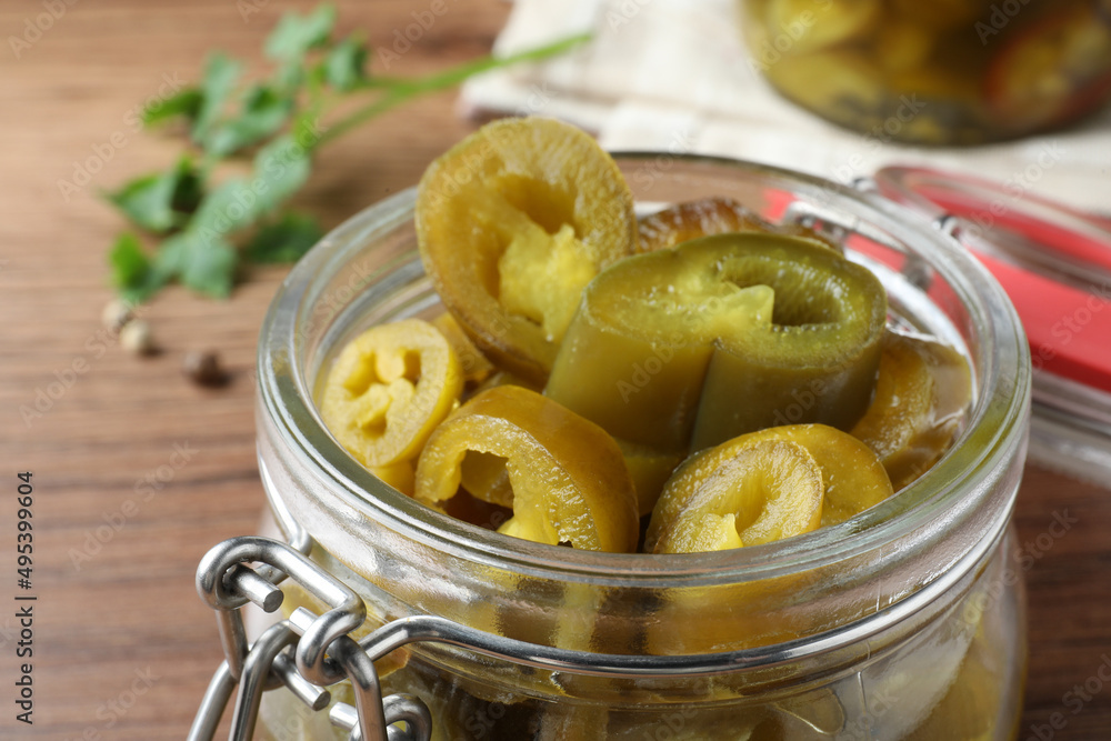 Glass jar with slices of pickled green jalapeno peppers on wooden table, closeup