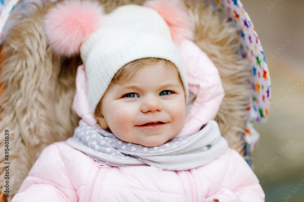 Cute little beautiful baby girl sitting in the pram or stroller on cold autumn, winter or spring day. Happy smiling child in warm clothes, fashion stylish baby coat and hat. Snow falling down Cute little beautiful baby girl sitting in the pram or stroller on cold autumn, winter or spring day. Happy smiling child in warm clothes, fashion stylish baby coat and hat. Snow falling down
