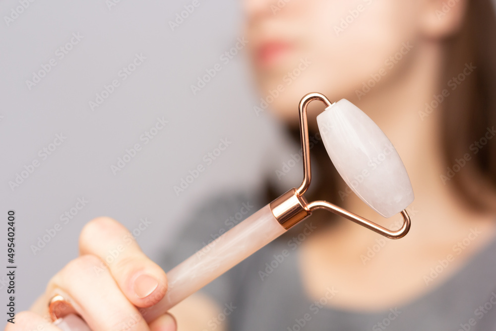 Closeup of a woman using a rose quartz roller to depuff her face in the morning.
