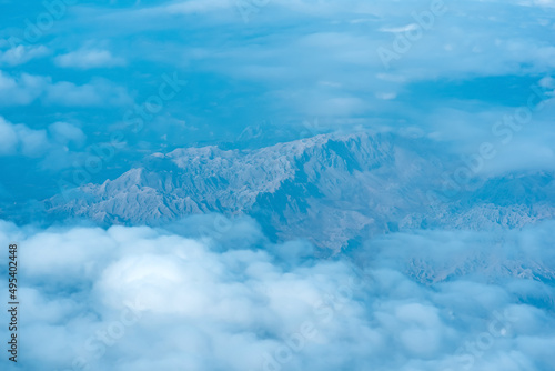 view of the earth below while flying above the clouds, mountainous terrain through atmospheric haze, view from above © Evgeny