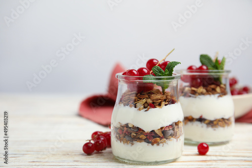 Delicious yogurt parfait with fresh red currants and mint on white wooden table, space for text