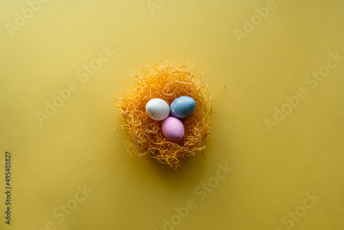 Nest with Easter eggs on yellow background with copy space for text.