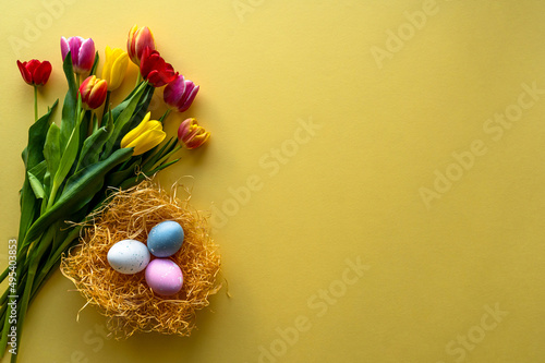 Stylish background with colorful Easter eggs isolated on yellow background with colorful tulip flowers. Flat lay, top view, mockup, overhead, template