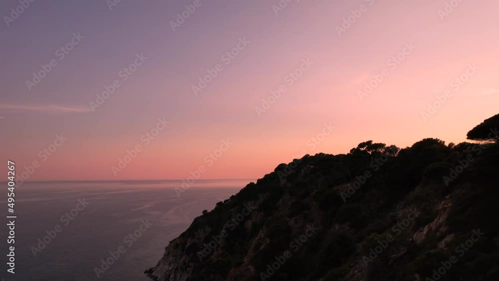 Aerial Along Silhouetted Coast Of Costa Brava Next To Mediterranean Sea With Orange Sunset Skies. Dolly Forward Aerial Along Silhouetted Coast Of Costa Brava Next To Mediterranean Sea With Orange Sunset Skies. Dolly Forward
