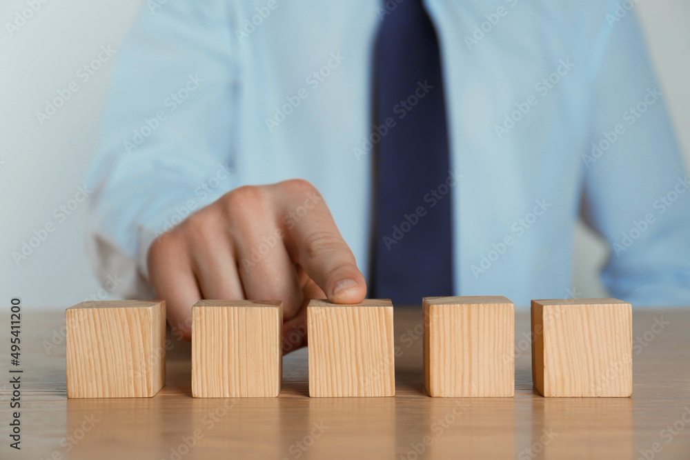 Businessman arranging blank cubes on wooden table, closeup. Space for text