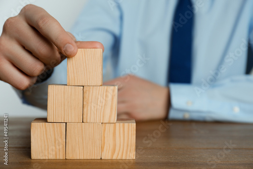 Businessman building pyramid of blank cubes on wooden table, closeup. Space for text