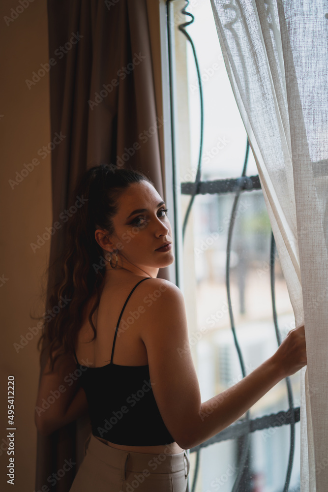 Chica joven delgada abriendo cortina en habitación de hotel Chica joven delgada abriendo cortina en habitación de hotel