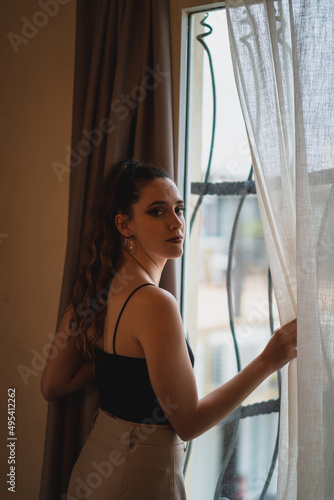 Chica joven delgada abriendo cortina en habitación de hotel